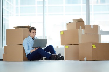 Mann sitzt am Boden im leeren Büro mit Umzugskartons