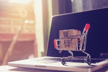 Modelleinkaufwagen vor einem PC als Zeichen für Online-Shopping